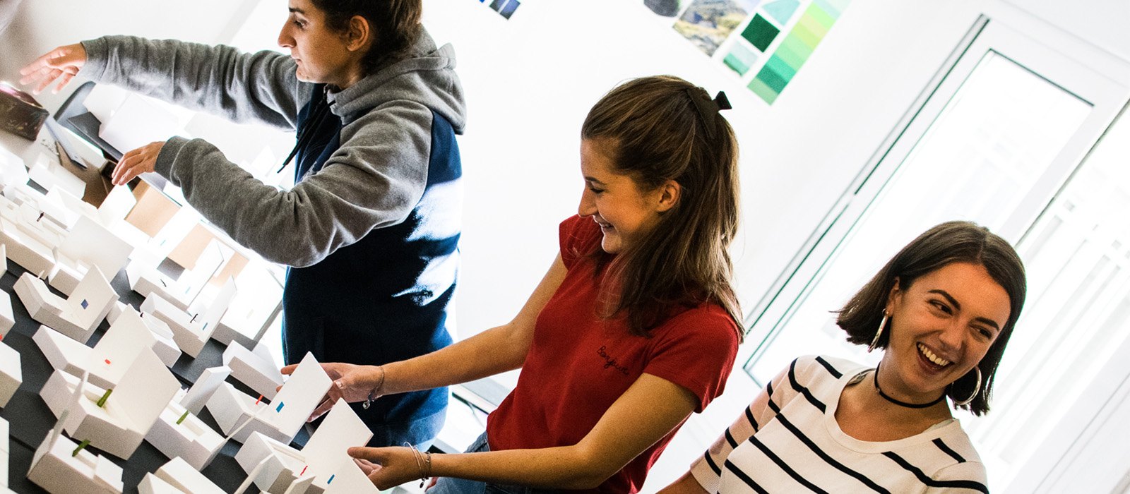 3 personnes souriantes travaillent ensemble sur une maquette architecturale